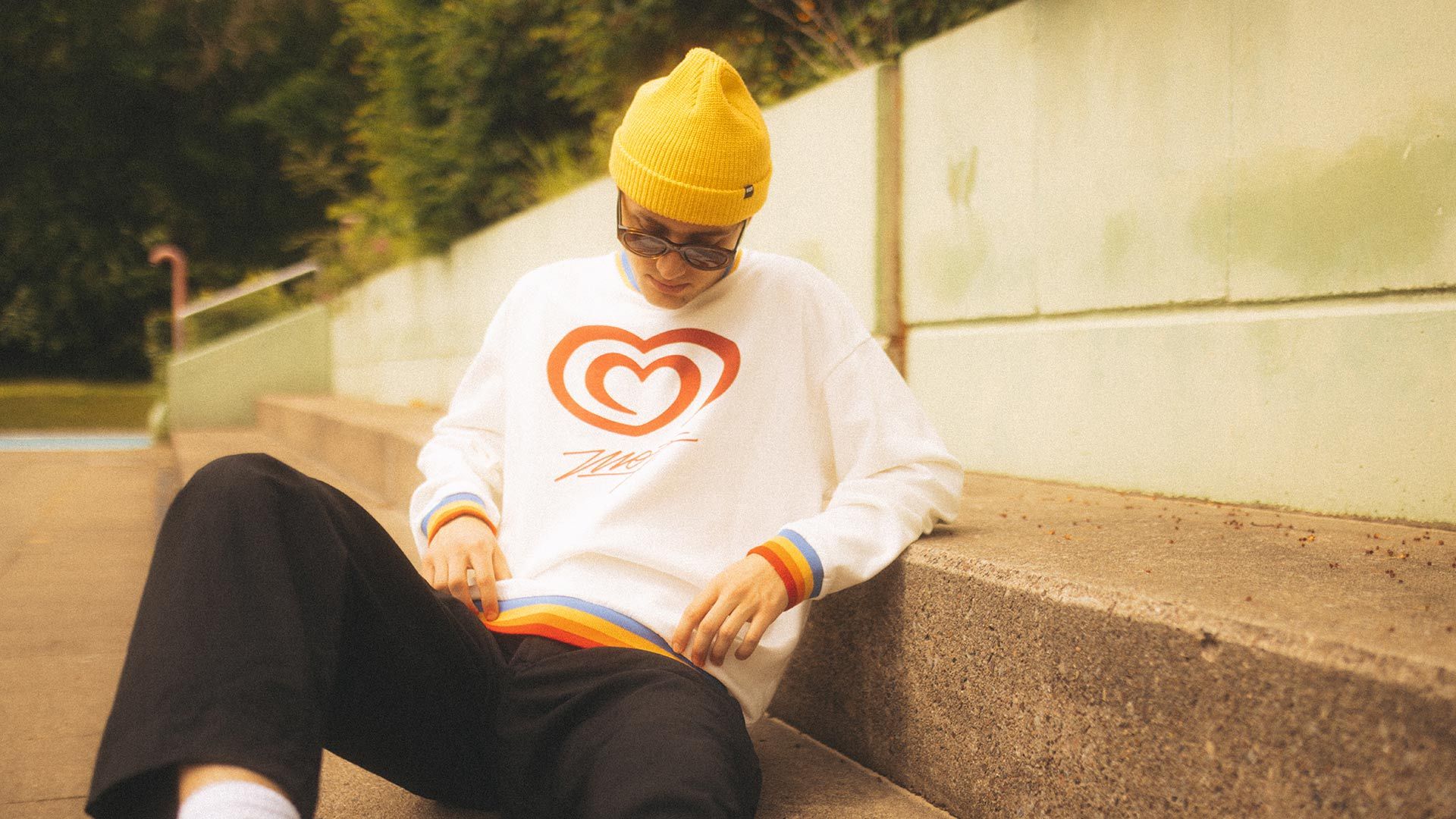 Ein junger Mann sitzt auf einer Treppe und hat ein Sweatshirt aus der Langnese-Mojo Kollektion an.