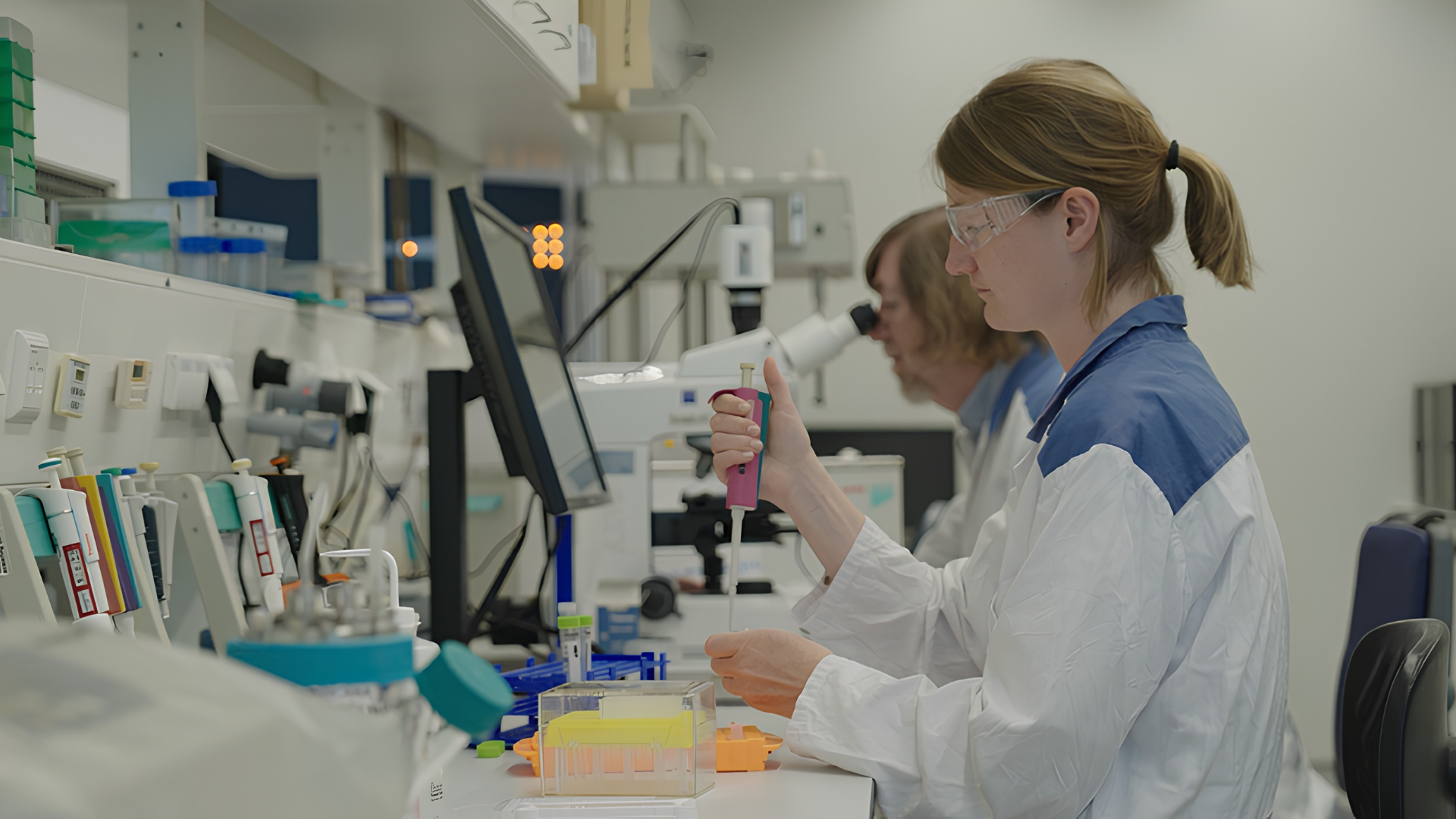 Eine Frau in einem Laborkittel und mit Schutzbrille benutzt eine Pipette.
