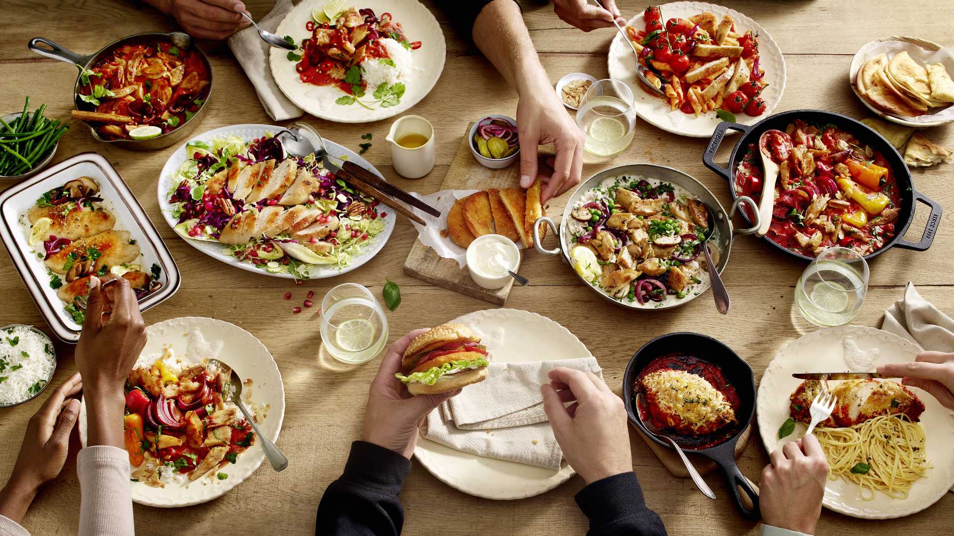 Ein reichhaltig gedeckter Holztisch mit veganen Burgern, Nudeln, Gemüse und pflanzenbasierten Fleischalternativen.