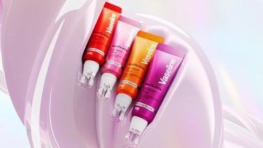 Vier Tuben Vaseline Gluta Hya Lip Serum in den Farben „Cherry Crush“, „Rosy Pink“, „Juicy Peach“ und „Royal Plum“ vor einem glänzenden, rosa Hintergrund.