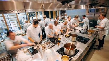 Ein Team von Unilever Food Solutions Köchen bereitet in einer lebhaften Küche Essen vor. Zahlreiche Töpfe stehen auf den Herdplatten.