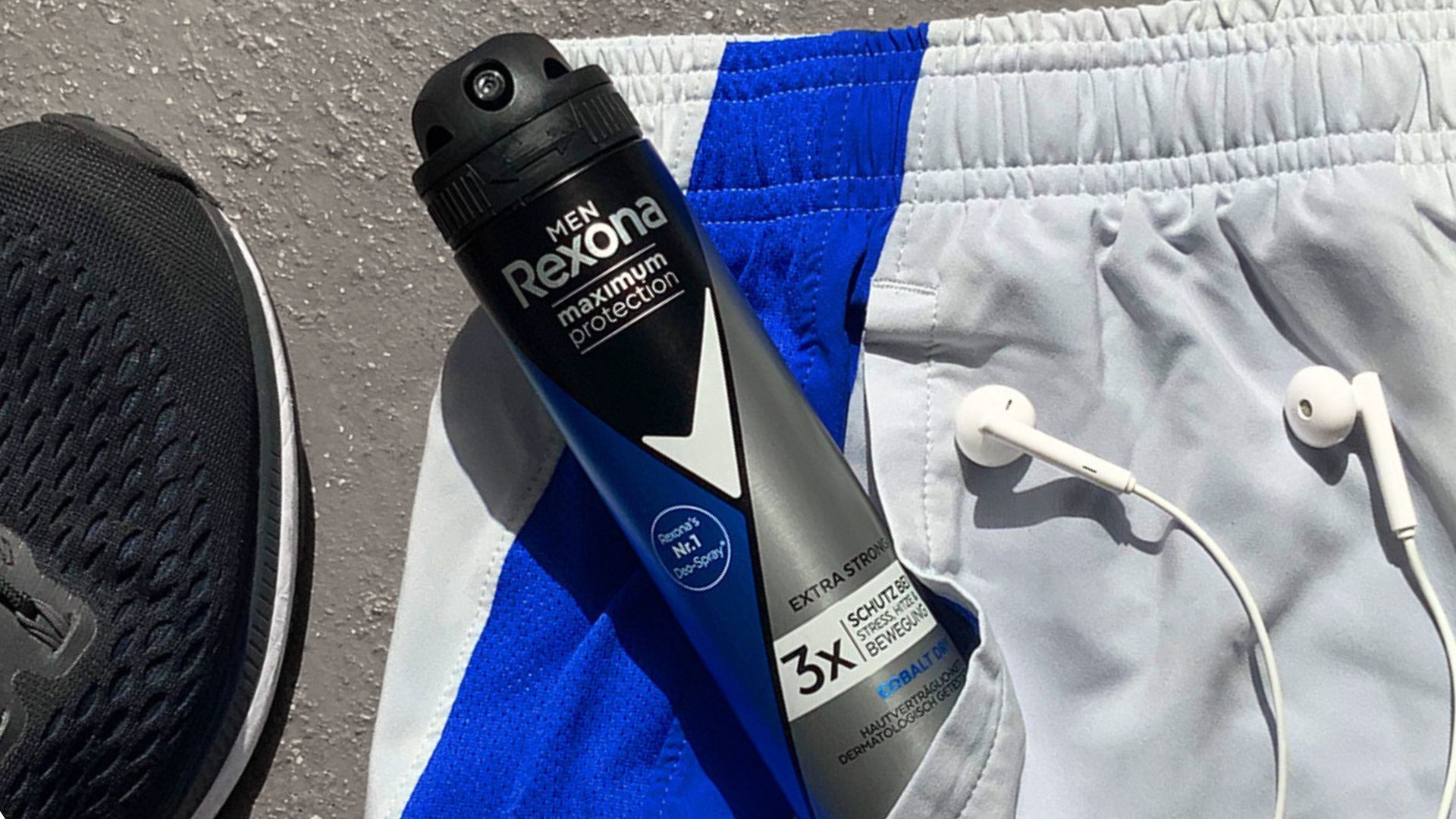Eine Nahaufnahme eines Rexona-Deodorants in der Tasche einer Turnhose, daneben ein Paar Kopfhörer und ein Tennisschuh.