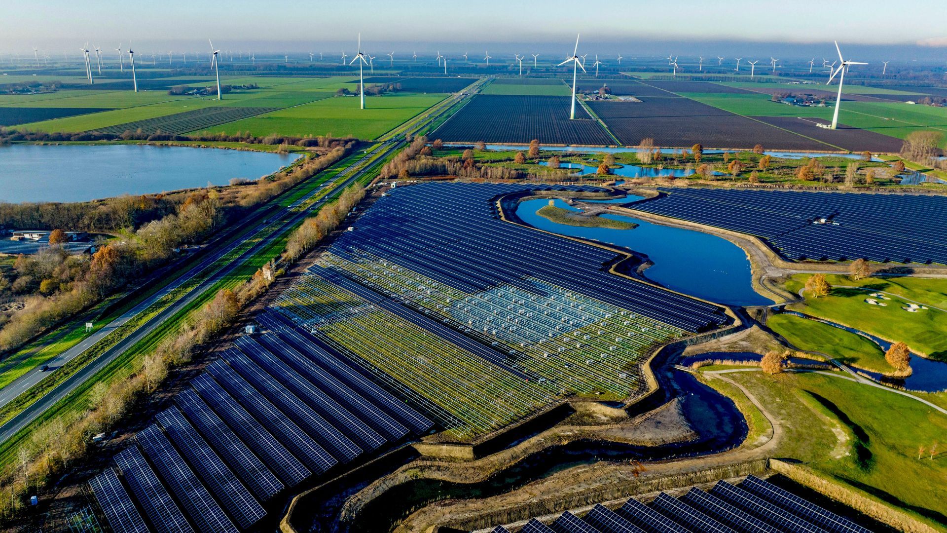 Luftaufnahme eines großen Solarparks und eines Windparks zwischen Feldern und Seen